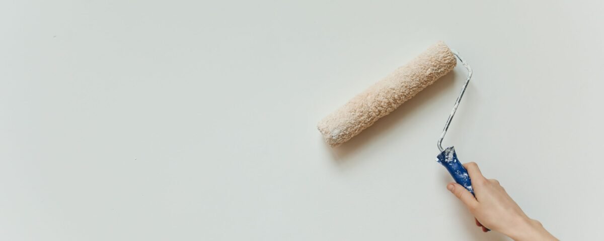 Close-up of a hand using a paint roller to apply fresh white paint to an interior wall