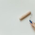Close-up of a hand using a paint roller to apply fresh white paint to an interior wall