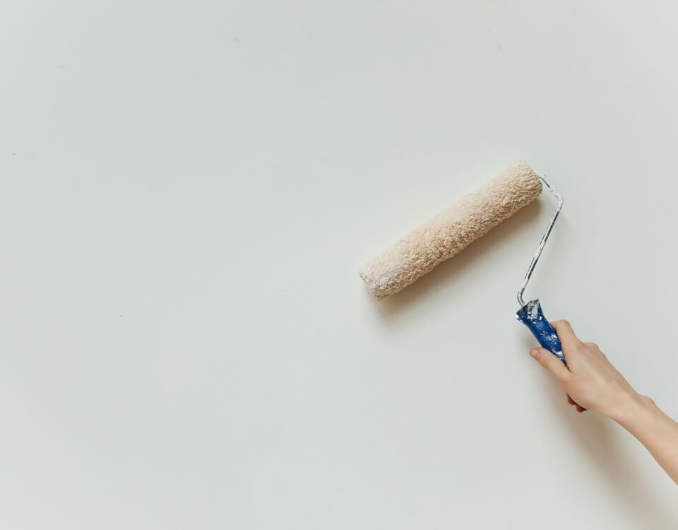 Close-up of a hand using a paint roller to apply fresh white paint to an interior wall
